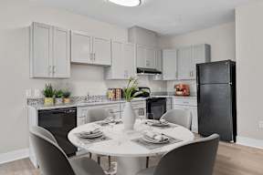 A kitchen with a table set for two and a black refrigerator.
