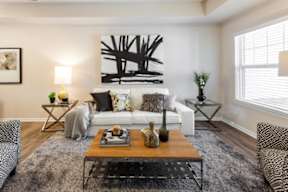 A living room with a white couch, a wooden coffee table, and a large abstract painting on the wall.