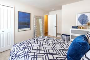 A bedroom with a patterned bedspread and a painting on the wall.