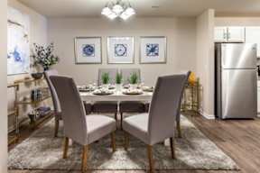 A dining room with a table set for four and a refrigerator in the background.