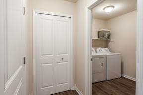 A white door is in a hallway with a washer and dryer in the other room.