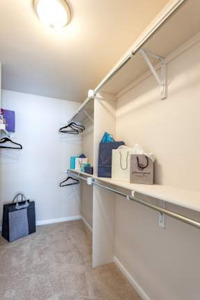 A white closet with clothes hanging and a bag on the floor.