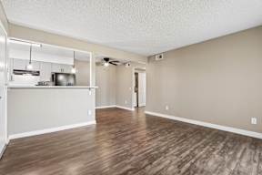 A room with wooden flooring and a kitchen area in the background.