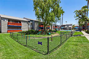 A playground with a black fence and a blue sign is surrounded by grass.