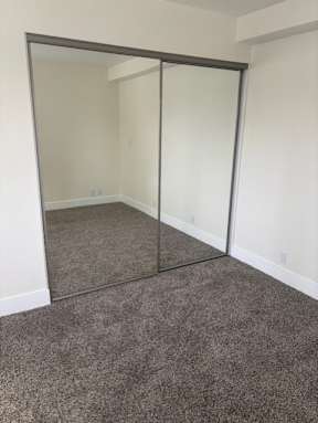 A room with a grey carpet and a large mirror.