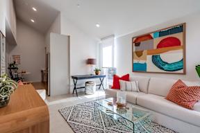 A modern living room with a white sofa and a colorful abstract painting on the wall.