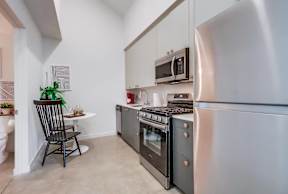 A kitchen with a black chair and a stainless steel refrigerator.