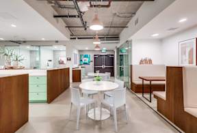 A modern office space with a glass wall and a white table with four chairs.