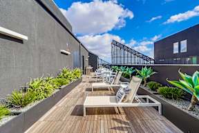 A modern balcony with wooden flooring and white lounge chairs.