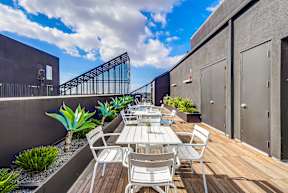 A patio with a table and chairs is surrounded by plants and a metal railing.