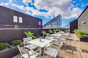 A patio with a table and chairs is surrounded by plants.