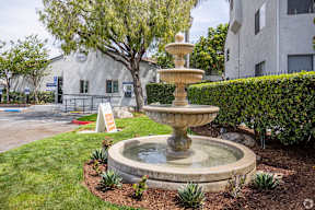 A stone fountain is in the middle of a grassy area.