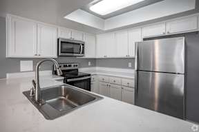 A kitchen with a stainless steel refrigerator, sink, and stove.