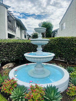 A fountain in the middle of a garden with a blue pool of water.