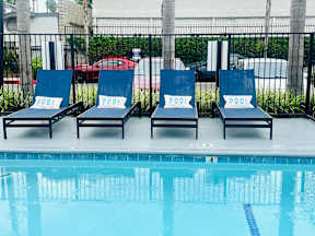 Four lounge chairs with the word "POOL" on them are arranged in a row by a pool.