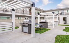 A patio with a grill and picnic table is surrounded by white balconies.