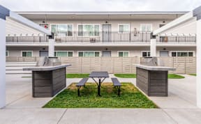 A concrete patio with a table and two benches in front of a building.