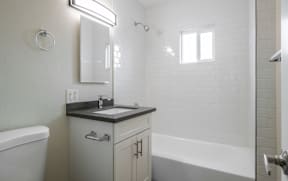 A white bathroom with a sink, mirror, and bathtub.