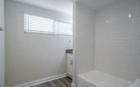 A white bathroom with a tub, sink, and window.
