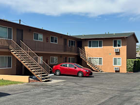 A red car is parked in front of a two-story apartment building.