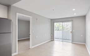 A spacious, empty room with a refrigerator on the left and a sliding glass door on the right.
