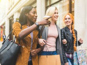 three young women walking down a street with shopping bags