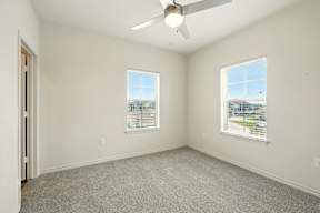 A room with a ceiling fan and two windows.