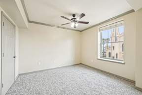 A room with a ceiling fan and a window overlooking a building.