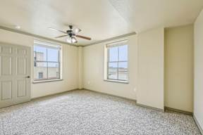 A room with a ceiling fan and two windows.