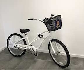 A white bicycle with a black bag on the handlebar.