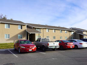 A red car is parked in a parking lot in front of a building at Grand Manor Apartments, Grand Junction, CO