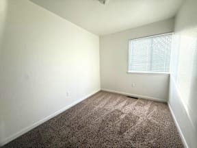 A room with a carpeted floor and a window with blinds.