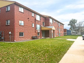A red brick building with a green lawn in front at Townview Plaza Apartments, Denver, CO, 80204.