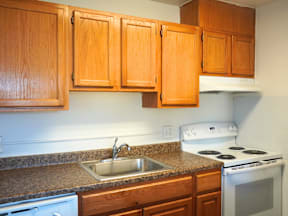 A kitchen with a stove, sink and cabinets at Garden Court Apartments, Denver