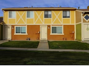 A yellow house with brown trim and a green door at Willow Grove Apartments, Clifton, Colorado.