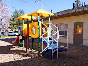 A playground with a yellow and green structure and a blue slide at Mountain Terrace Apartments, Westminster, CO, 80031.