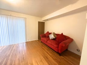 A red couch with two pillows sits in a room with wooden floors and a sliding glass door.