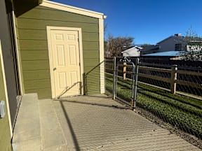 A small green building with a white door and a metal fence at Willow Grove Apartments, Clifton, CO.