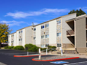 A parking lot in front of a building with a blue handicap parking sign at Garden Court Apartments, Denver, CO, 80220