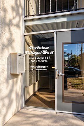 The entrance to a private property with a glass door and a sign that reads "Parkview Village West".