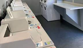 A row of white washing machines are lined up in a laundromat.