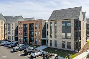 A parking lot with cars and a building with a mix of brick and siding exterior.