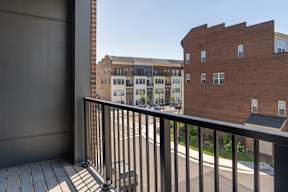 A balcony with a black railing overlooks a street with buildings.