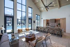 A modern living room with a bar area and a view of the outdoors through large windows.