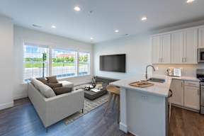 A modern living room with a grey sofa and a white kitchen.