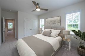 A bedroom with a large bed, a ceiling fan, and a painting on the wall.