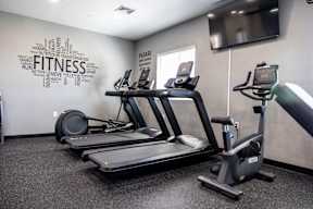 A fitness room with a treadmill, elliptical trainer and a wall with fitness related words.