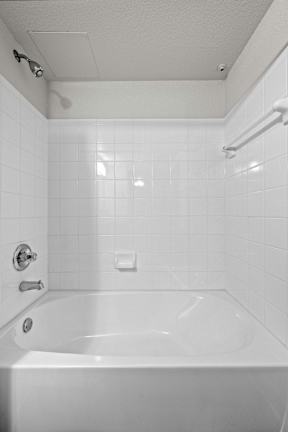 A white bathroom with a white tub and white tiles.