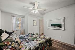 A bedroom with a floral bedspread and a white ceiling fan.