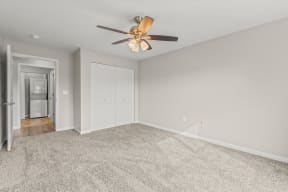 an empty living room with a ceiling fan and a door to a kitchen